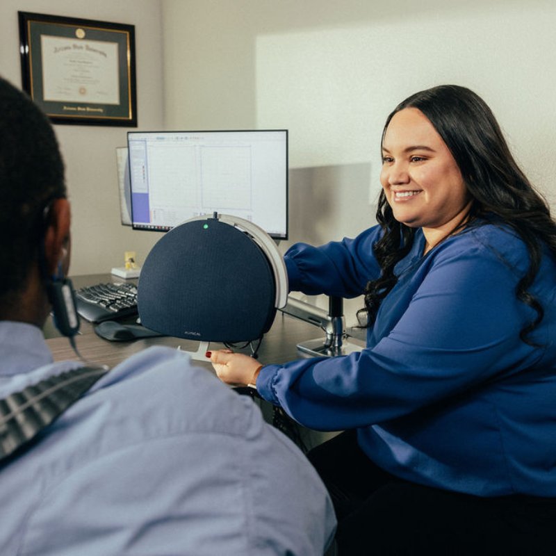 Dr. Balderas smiling at a patient across her desk while adjusting a speaker used for hearing testing