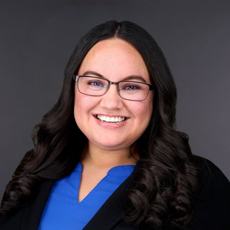 Dr. Leslie Balderas, audiologist, smiling in glasses, a royal blue blouse and a black blazer